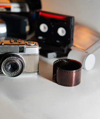 Vintage Camera and Film Roll with Retro Equipment A vintage camera with a roll of film beside it, surrounded by various old photographic equipment and cassette tapes. The scene captures a nostalgic vibe of analog photography and music.